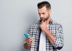 Photo of young handsome serious thoughtfuk minded man thinking hold cellphone isolated on grey color background